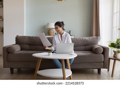 Young Happy Indian Woman Read Paper Notice With Good News Smiling Seated On Sofa At Tablet With Laptop, Feels Satisfied With Bank Statement, Money Refund, Enough Of Earnings For Life. Finance, Savings