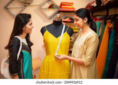 Young happy indian woman,tailor seamstress,smiling fashion designer showing customer or client dress measurements with tape,measuring on mannequin,standing in garment workshop,atelier or studio. - Powered by Shutterstock