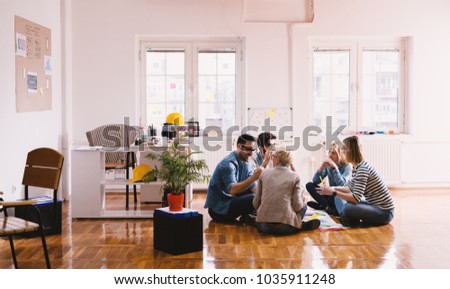 Young happy innovative business people sitting on the floor of the office in the circle and brainstorming with pleasure. Teamwork and togetherness concept.