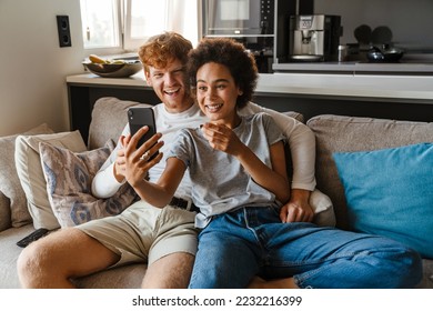 Young happy interracial couple taking selfie with phone together , while sitting on couch in cozy living room at home - Powered by Shutterstock