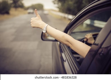 Young Happy Lady Driving A Car And Making Like /  Ok Sign With Hand Out Of Window. Girl Driving And Enjoying Road Trip And Travel, Toned With Soft Autumn Colors.