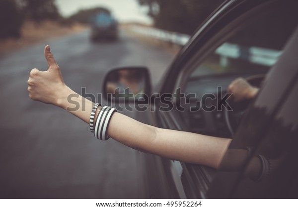 Young\
happy lady driving a car and making Like / Ok sign with hand out of\
window. Girl driving and enjoying road trip and travel. Freedom and\
happiness concept. Old fashioned sepia\
colors.