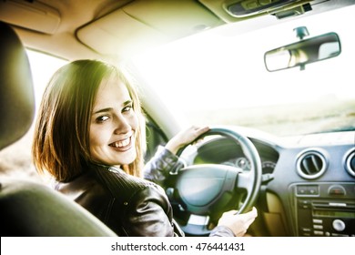 young happy latin hispanic woman driving a car. Smiling girl driver seated behind the steering wheel of her auto looking out at rear passengers