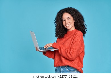 Young happy latin woman using laptop device isolated on blue background. Smiling female model user holding computer presenting advertising job search or shopping website, online services concept.