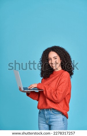 Young happy latin woman using laptop device isolated on blue background. Smiling female model user holding computer presenting advertising job search or shopping website, online services, vertical.