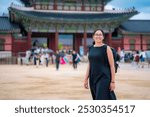 Young happy Latina woman in a black dress and backpack smiling near Gwanghwamun Gate in Seoul, South Korea.