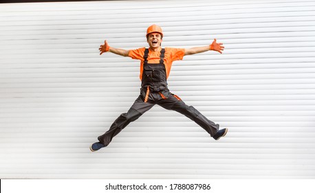 Young happy laughing caucasian man builder construction worker in a safety helmet is jumping in front of the roller door lifting gates. Copy space for you text and logo. Industry concept - Shutterstock ID 1788087986
