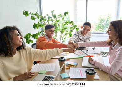 Young happy laughing creative startup team four multiethnic coworkers diverse students work together give fist bump celebrate successful project in office classroom at desk. Teamwork success concept.