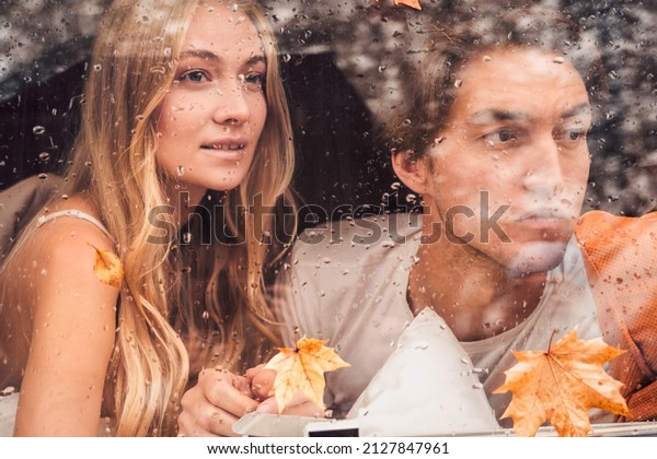 Young happy lovers couple behind wet
misted window,rain drops.Drawing heart with finger.Autumn
atmosphere,mood,maple leaves.Love romantic road travel. Traveling
in camper,house on
wheels,trailer.