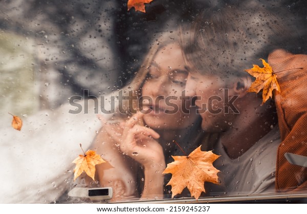Young happy lovers couple behind wet\
misted window,rain drops.Drawing heart with finger.Autumn\
atmosphere,mood,maple leaves.Love romantic road travel. Traveling\
in camper,house on\
wheels,trailer.