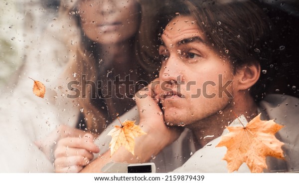 Young happy lovers couple behind wet\
misted window,rain drops.Drawing heart with finger.Autumn\
atmosphere,mood,maple leaves.Love romantic road travel. Traveling\
in camper,house on\
wheels,trailer.