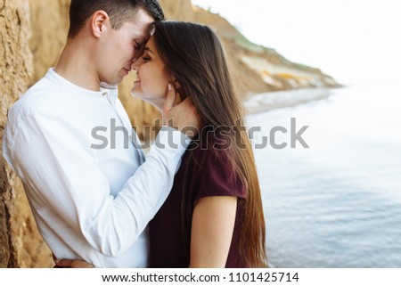 young, happy, loving couple, near the sand wall, on the sea, in the arms, and look at each other,