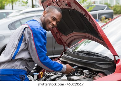 Young Happy Male Mechanic Testing Car Battery With Multimeter