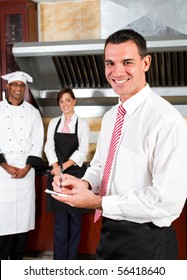 young happy male restaurant manager and his staff in kitchen