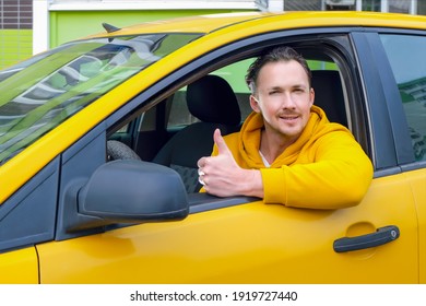 Young happy male taxi driver sits behind the wheel of a taxi and shows like