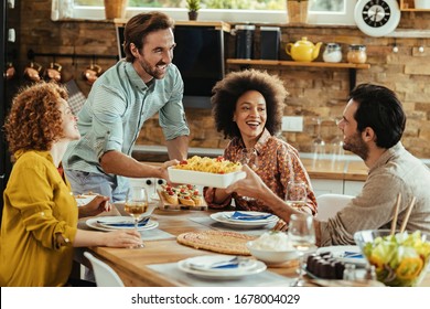 Young happy man bringing food at the table while having lunch with friends at home. - Powered by Shutterstock