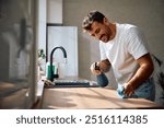 Young happy man cleaning kitchen counter at home. Copy space. 