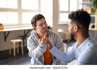 Young happy man with Down syndrome with his mentoring friend celebrating success indoors at school. - Shutterstock ID 2063272721