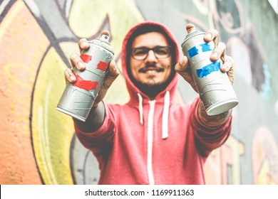 Young Happy Man Drawing With Two Smiling Sprays  - Graffiti Artist Painting With Aerosol Color Cans On The Wall - Urban Lifestyle, Youth, Millennial Generation And Street Art Concept - Focus On Bottle