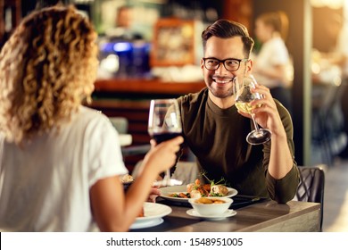 Young Happy Man Drinking Wine And Talking To His Girlfriend While Having Lunch In A Bar. 