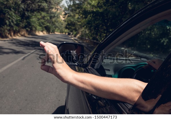 Young\
happy man drives a car and holds his hand out from the window.\
Driver enjoys driving and shows Ok Happy  sign with his hand out of\
window. Road trip, travel and freedom\
concept.