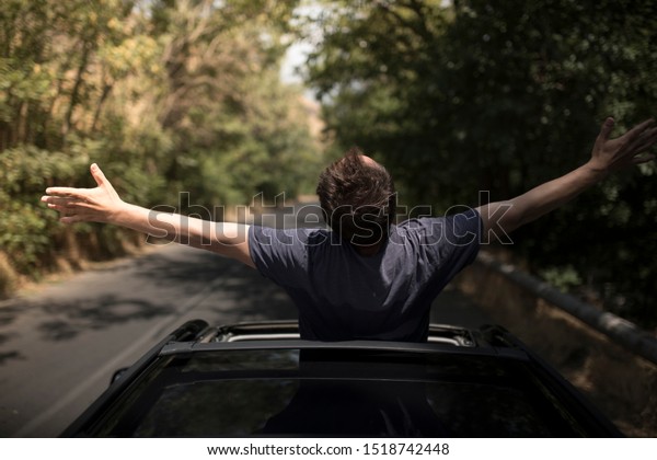 Young\
happy man drives a car and holds his hand out from the window.\
Driver enjoys driving and shows Ok Happy  sign with his hand out of\
window. Road trip, travel and freedom\
concept.