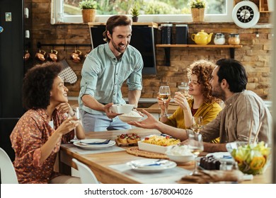 Young happy man having lunch with his friends and serving food at dining table.  - Powered by Shutterstock