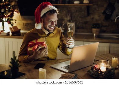 Young happy man having video call over laptop and toasting with Champagne while celebrating Christmas alone at home.  - Powered by Shutterstock