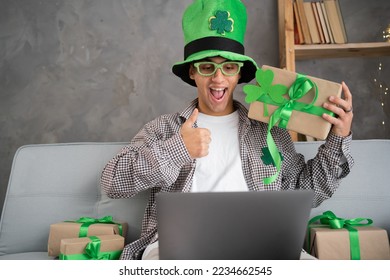 Young happy man having video call over laptop while celebrating St.Patrick's Day alone at home. Thumbs up gesture, happy young man in green hat - Powered by Shutterstock