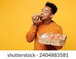 Young happy man he wears orange sweatshirt casual clothes holding italian pizza in cardboard flatbox isolated on plain yellow background. Proper nutrition healthy fast food unhealthy choice concept