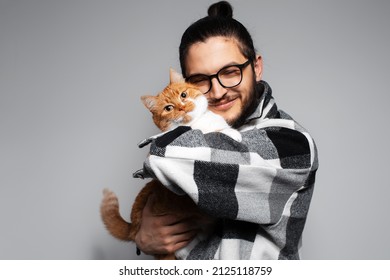 Young happy man hugs a red-white cat on grey background. Studio portrait.