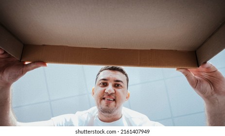 Young Happy Man Opening Cardboard Box After Relocation And Looking Inside Kissing In New House.