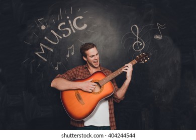 Young happy man play on guitar and singin against the background of chalkboard