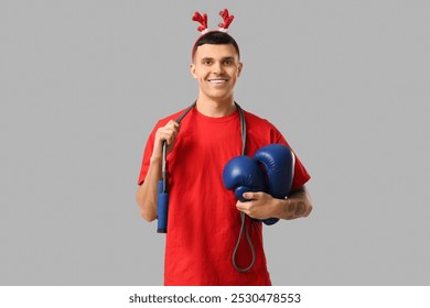 Young happy man in reindeer horns with skipping rope and boxing gloves on grey background - Powered by Shutterstock