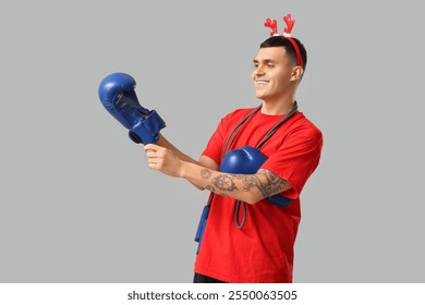 Young happy man in reindeer horns with skipping rope and boxing gloves on grey background - Powered by Shutterstock