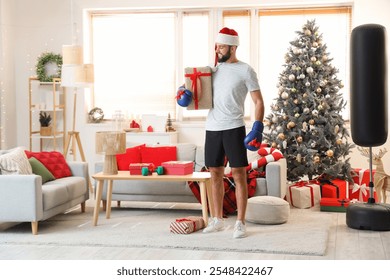 Young happy man in Santa hat with gift box and new boxing gloves at home decorated for Christmas - Powered by Shutterstock