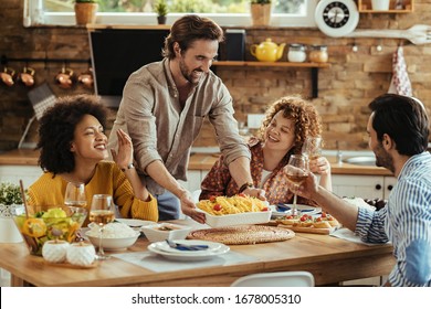 Young happy man serving food at dining table while having lunch with friends at home.  - Powered by Shutterstock