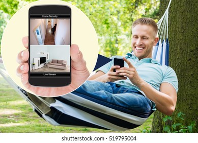 Young Happy Man Sitting On Hammock Looking At Home Security System On Mobilephone