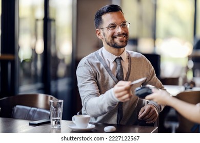 A young happy man in smart casual is sitting in coffee shop and paying with cashless technology with credit card in coffee shop. - Powered by Shutterstock