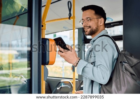 Young happy man using mobile phone while paying for a bus fare. 