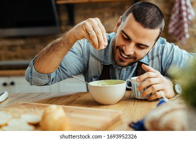 Young happy man using salt while preparing food in the kitchen.  - Powered by Shutterstock