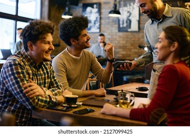 Young happy man using smart watch while making contactless payment to a waiter in a pub.  - Powered by Shutterstock