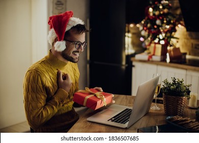 Young happy man virtually exchanging Christmas gifts while having video call over a computer at home.  - Powered by Shutterstock