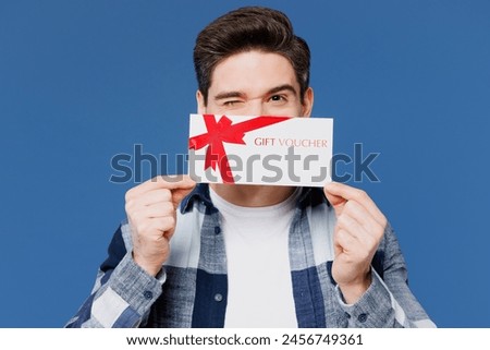 Young happy man wear shirt white t-shirt casual clothes hold cover mouth with gift certificate coupon voucher card for store isolated on plain blue cyan background studio portrait. Lifestyle concept