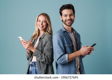 Young Happy Man And Woman Smiling And Using Mobile Phones Isolated Over Blue Background