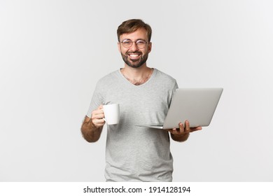 Young Happy Man Working With Laptop, Drinking Coffee And Smiling, Standing Over White Background