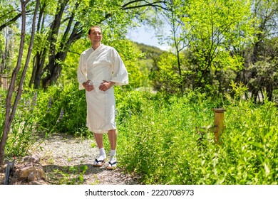 Young Happy Man In Yukata White Robe Spa Costume Or Gown Standing In Outdoor Garden In Japan With Nature View