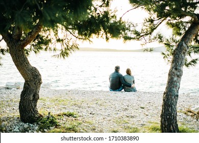 Young Happy Married Couple In Love Seating At Seaside Watching Sunset. Lifestyle Honeymoon Background, Copy Space. Digital Detox. Staycation. Romantic Concept. Close Up Man And Woman Holding Hands. 