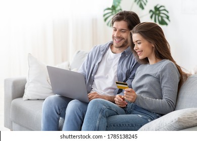 Young happy married couple making shopping online together at home, using credit card and laptop, copy space