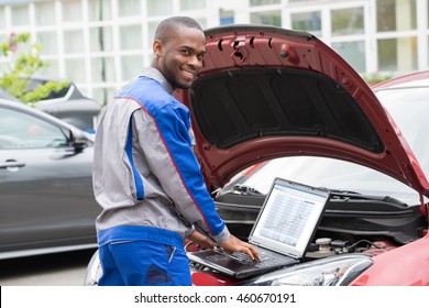 Young Happy Mechanic Using Laptop In Front Of Open Car Engine